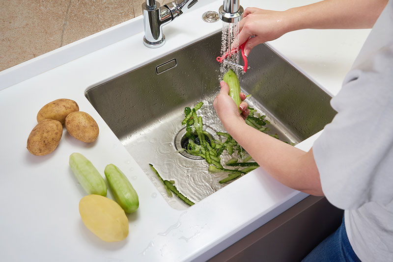 Residential owner peeling cucumbers into a garbage disposal in the sink